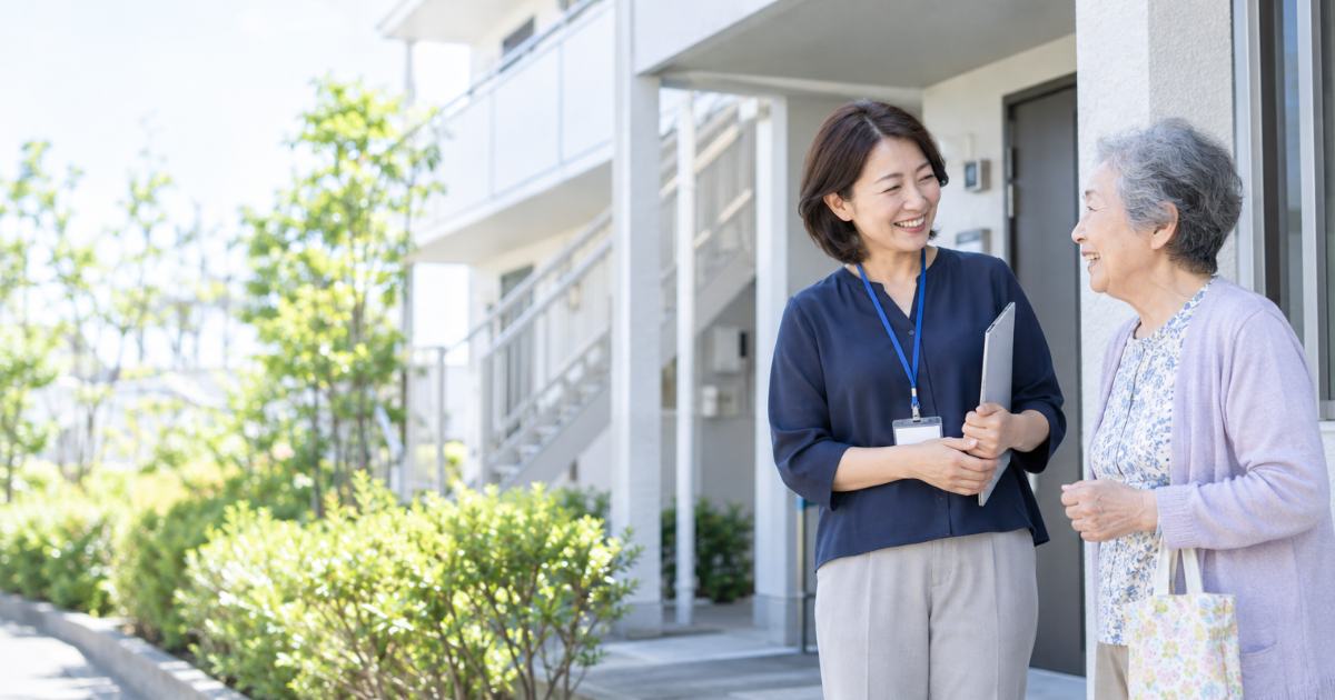 賃貸住宅の管理会社スタッフと高齢の入居者が玄関先で笑顔で話している写真イメージ